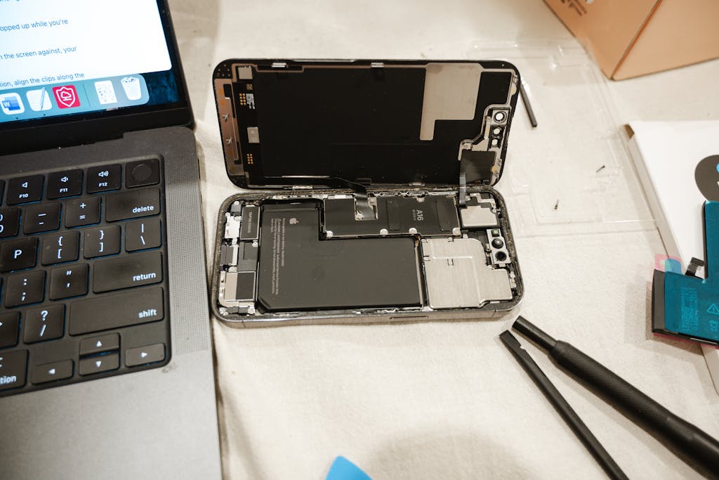 Open iPhone with repair tools and laptop, showcasing DIY battery replacement process.
